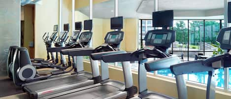 Un gimnasio con cintas de correr y elípticas, ventanas amplias y vistas a una piscina.
