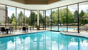 A swimming pool with clear blue water, surrounded by large windows offering views of trees and a building. - Marriott at the University of Dayton (Dayton)