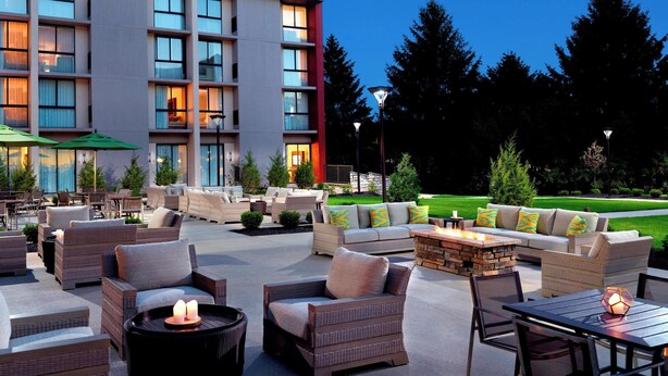 An outdoor patio area with wicker furniture, a fire pit, and a view of a hotel building. - Marriott at the University of Dayton (Dayton)