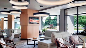 A modern hotel lobby with a large seating area, a TV mounted on the wall, and large windows offering a view of the outdoors. - Marriott at the University of Dayton (Dayton)