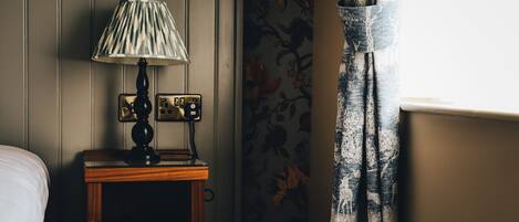 Een houten nachtkastje met een lamp, een stopcontact en een wandcontactdoos.