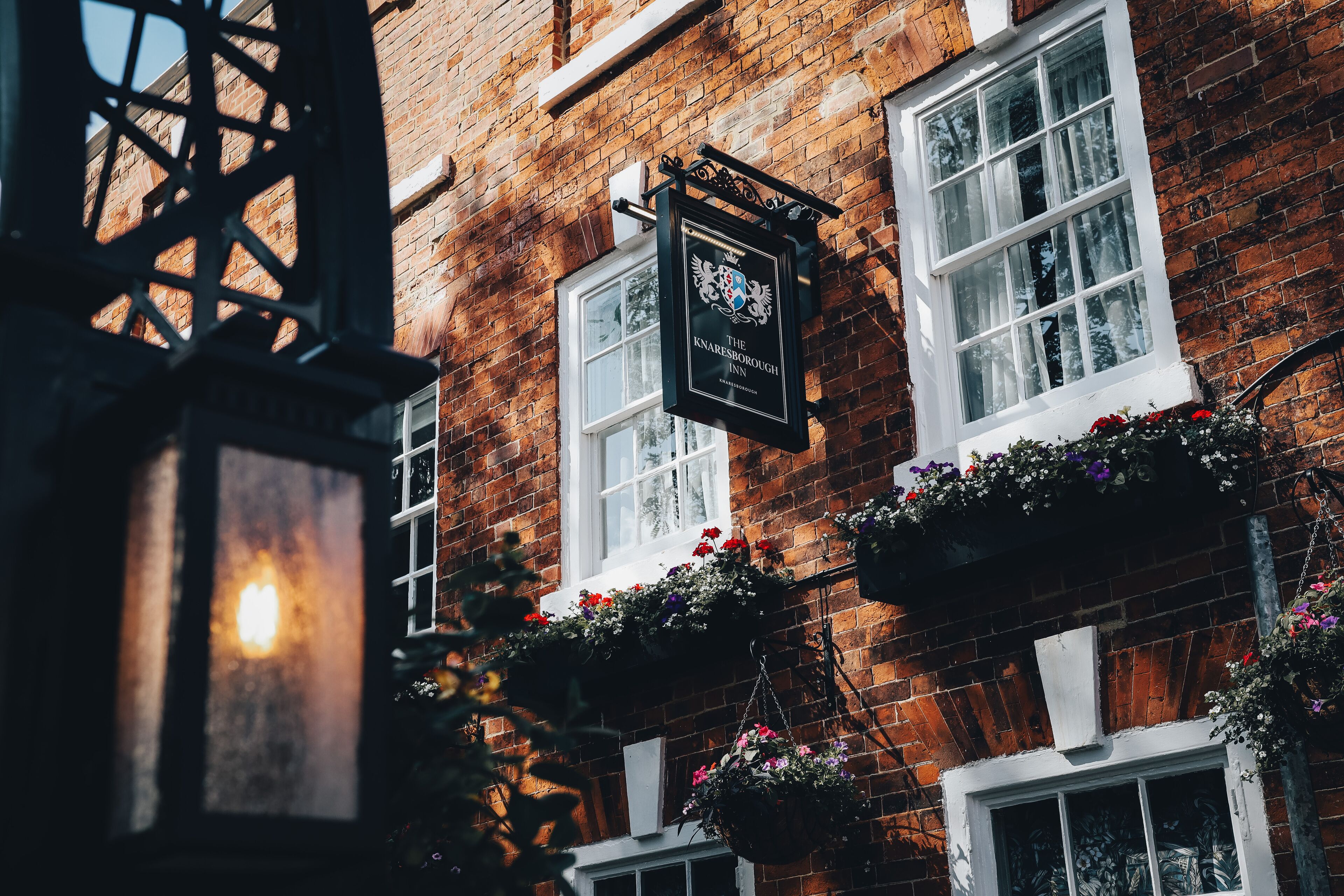 A brick building with a pub sign, windows with white frames, and hanging flower baskets.