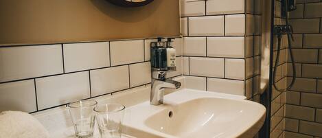 A bathroom with a white sink, two glasses, a towel, and a shower area.