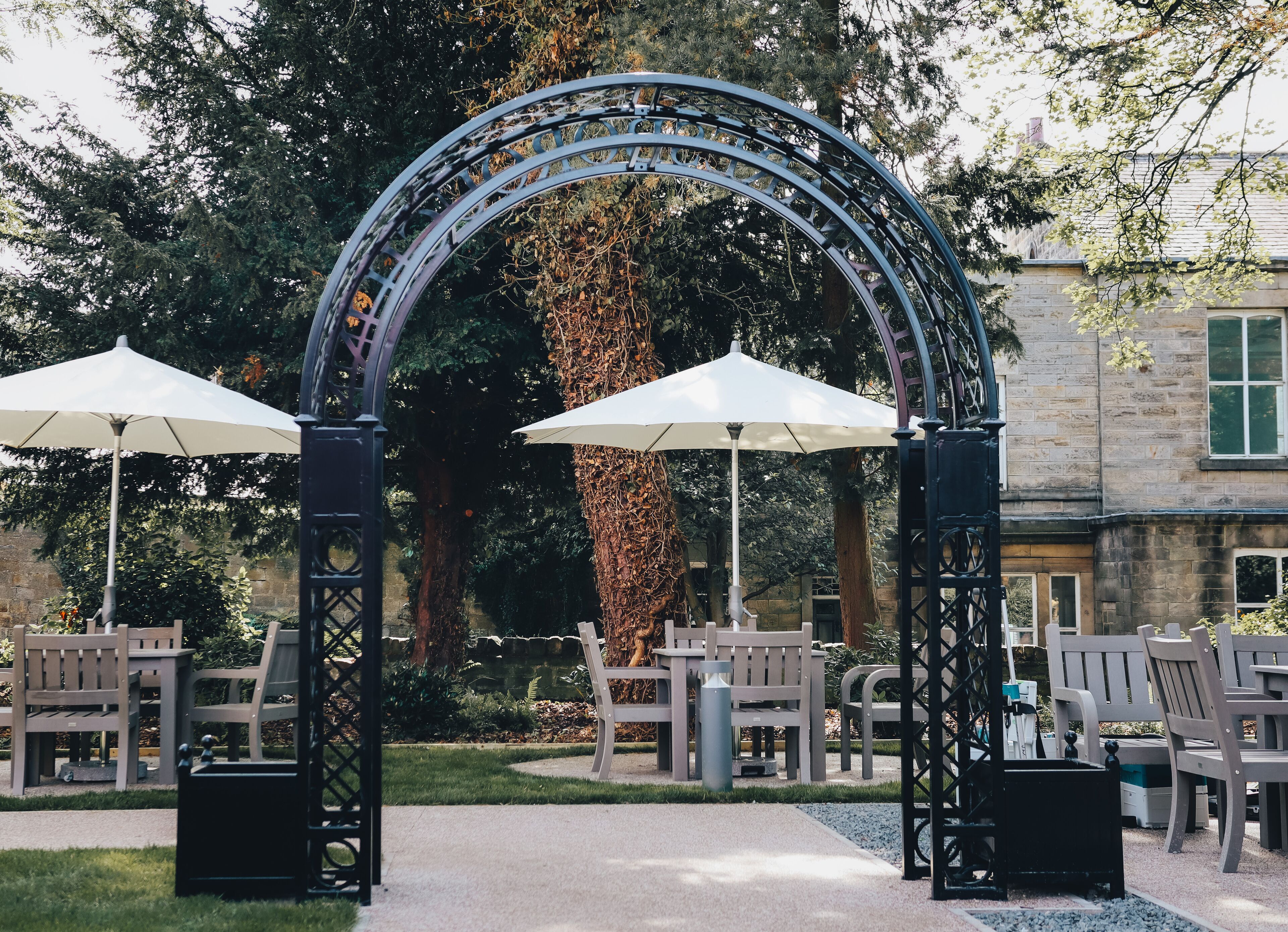 Un espacio al aire libre con un arco de metal, bancos y sombrillas.