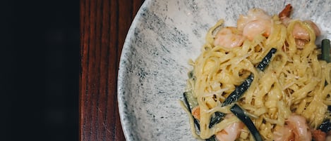 Un plato de pasta con camarones y vegetales sobre un plato de cerámica con motas.