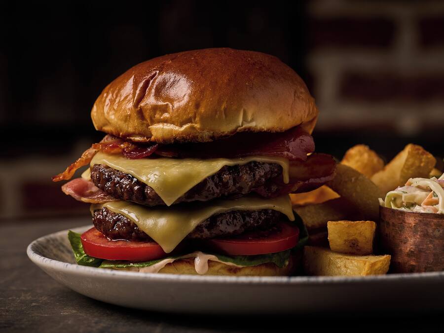 A burger with bacon, cheese, and tomato on a bun, served with fries and a side salad.