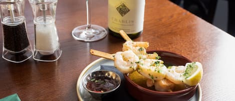 A plate of shrimp skewers with lemon and herbs, a bottle of wine, and two salt and pepper shakers on a wooden table.