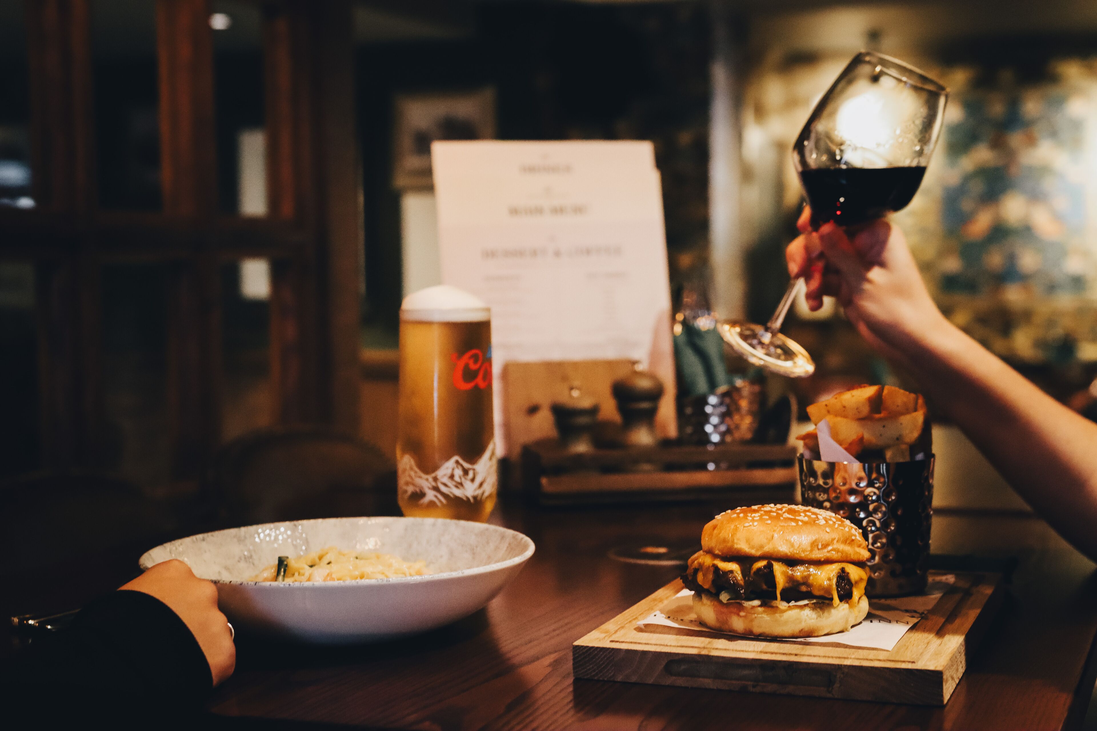 Una mesa de comedor con una hamburguesa, una copa de vino tinto, una jarra de cerveza y un menú.