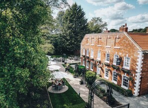 A brick building with a garden patio area, outdoor seating, and a pathway leading to the entrance. - The Knaresborough Inn - The Inn Collection Group (Knaresborough)