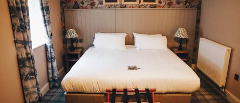 A neatly made bed with white linens, a plaid floor, and a wooden bench at the foot of the bed.