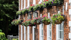 Un edificio de ladrillo tradicional con un letrero que dice “The Knareborough Inn”. Hay cestas de flores colgando de las ventanas y un seto bien cuidado a lo largo del camino.