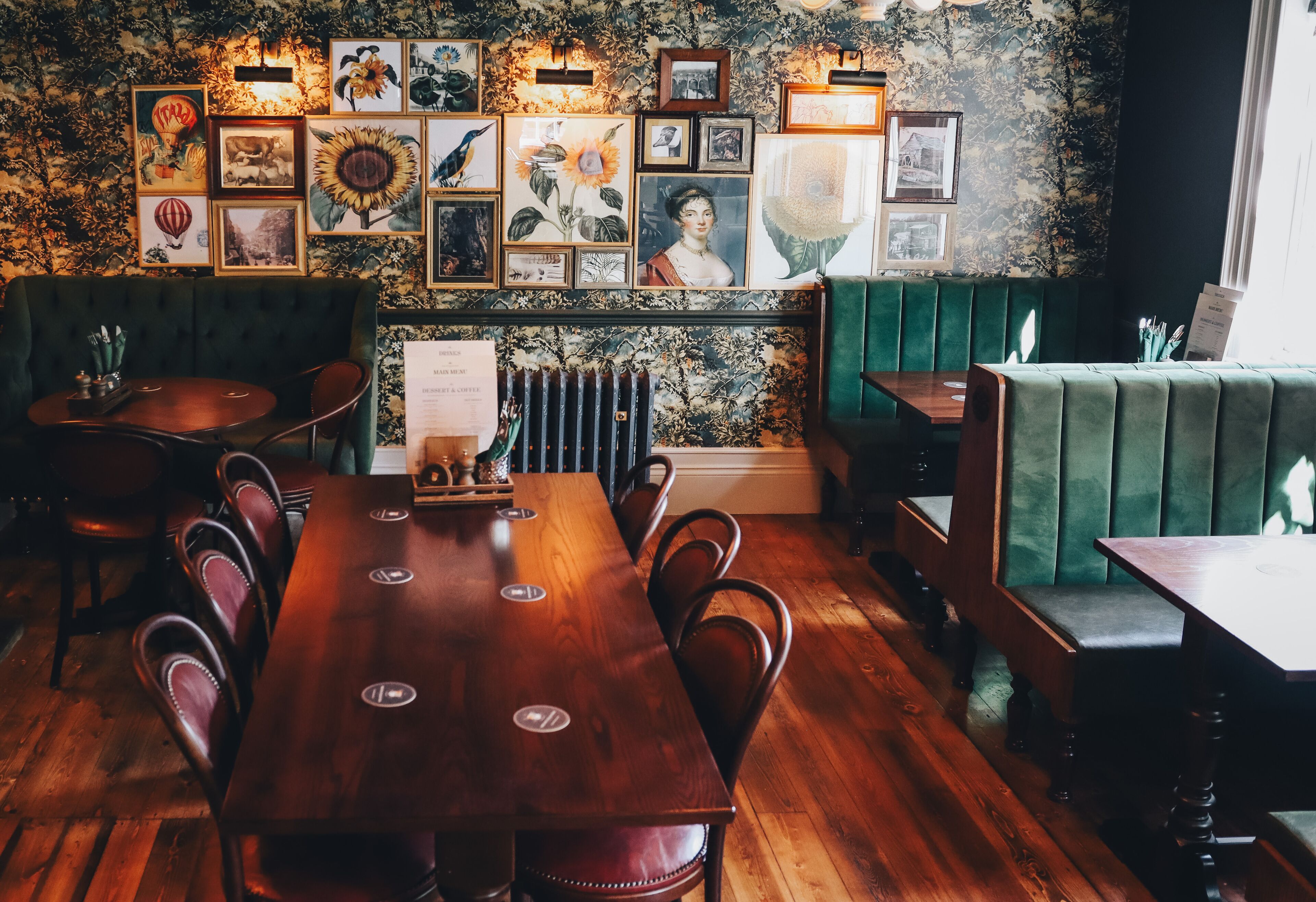 Un restaurante con una mesa de madera y asientos tapizados en verde, obras de arte en la pared y un radiador debajo.