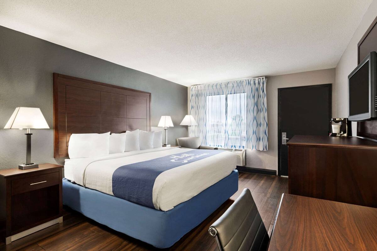 A hotel room with a large bed, two bedside tables with lamps, a desk with a television, and a window with curtains.