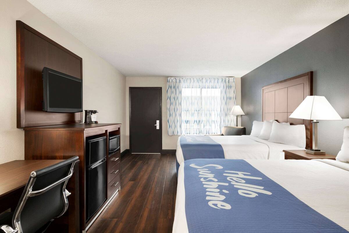 A hotel room with a bed, a desk, a chair, a television, and a window with curtains.