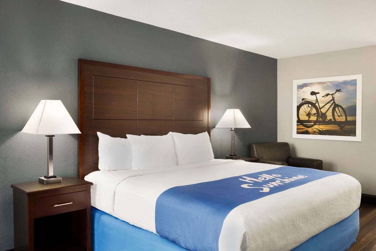 A hotel room with a large bed, two bedside lamps, a chair, a framed picture on the wall, and a blue and white bedspread.