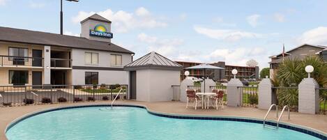 Un hotel Days Inn con piscina, mobiliario exterior y cielo despejado.