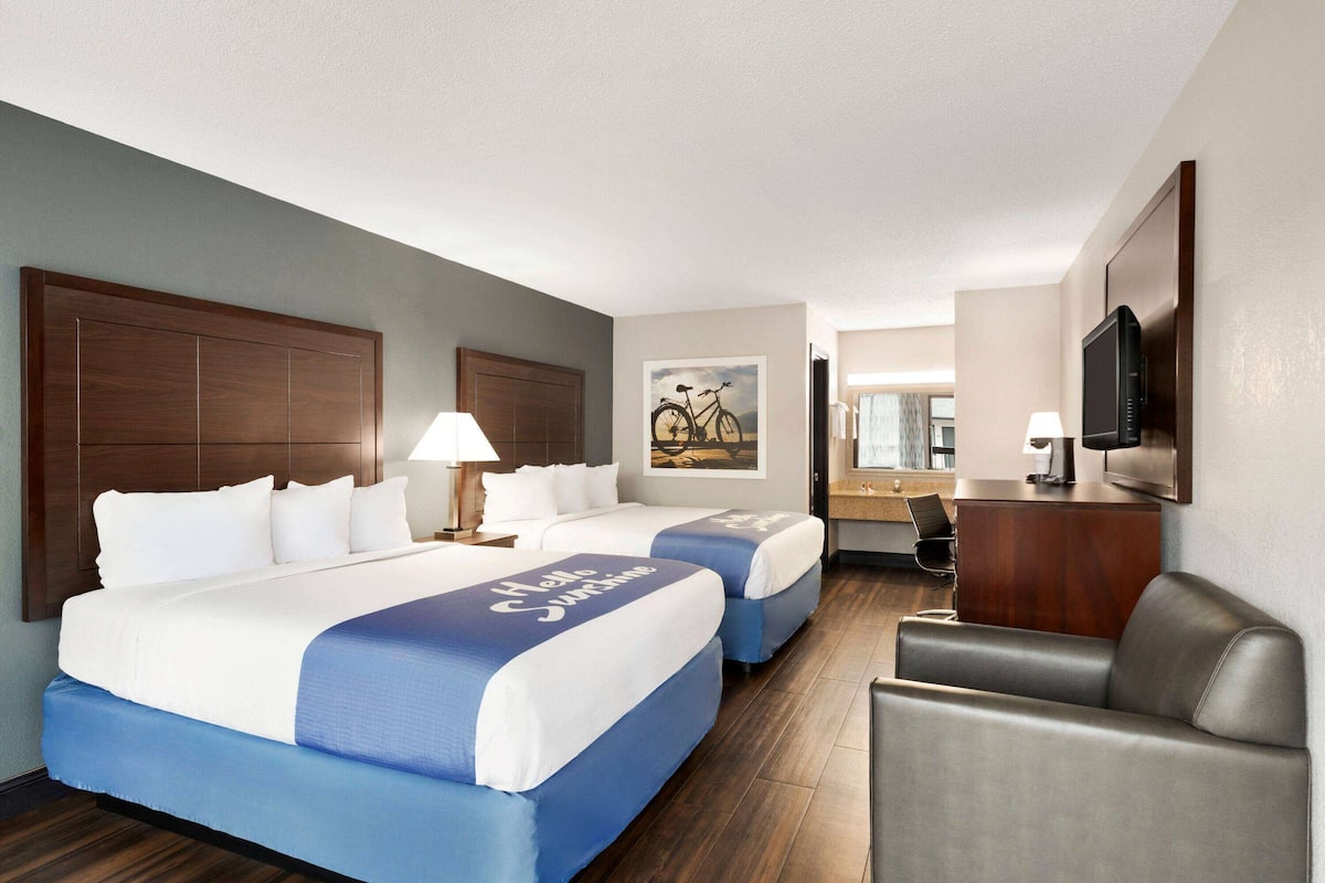 A hotel room with two beds, a desk, a chair, a TV, and a painting on the wall.
