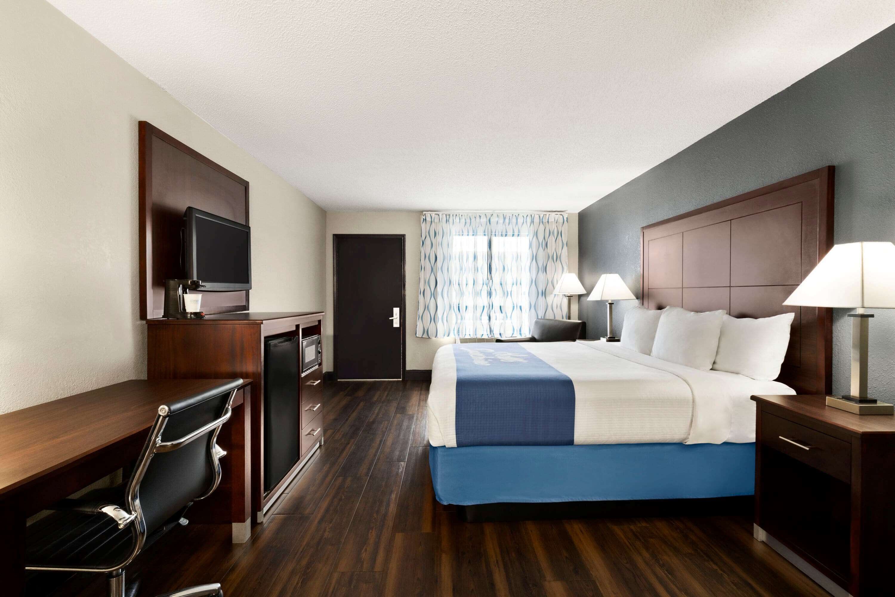 A hotel room with a bed, desk, chair, television, and lamps.