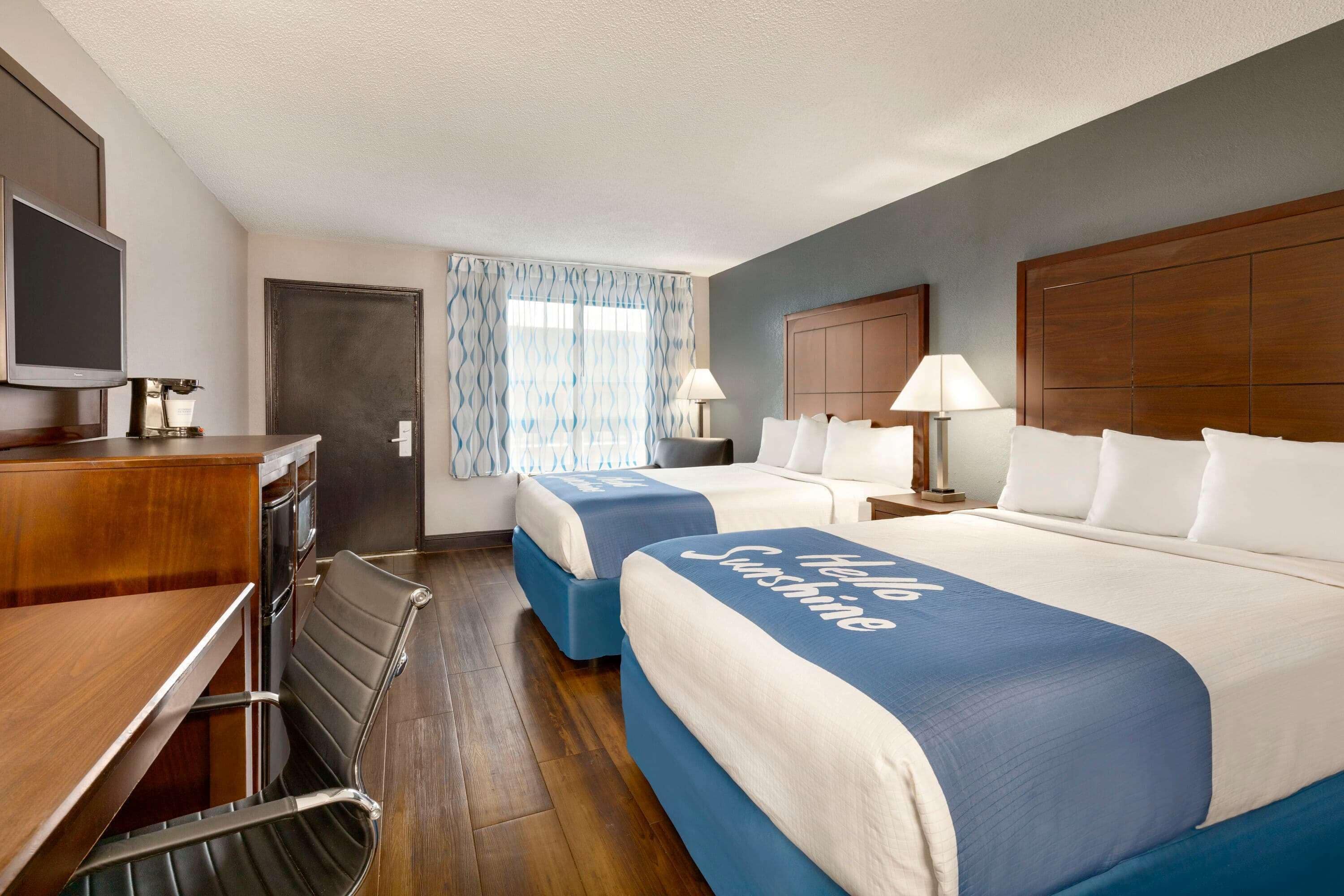 A hotel room with two beds, a desk, a television, and a window with curtains.