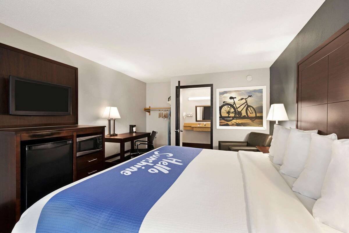 A hotel room with a large bed, a desk, a television, a mirror, and a bicycle painting on the wall.