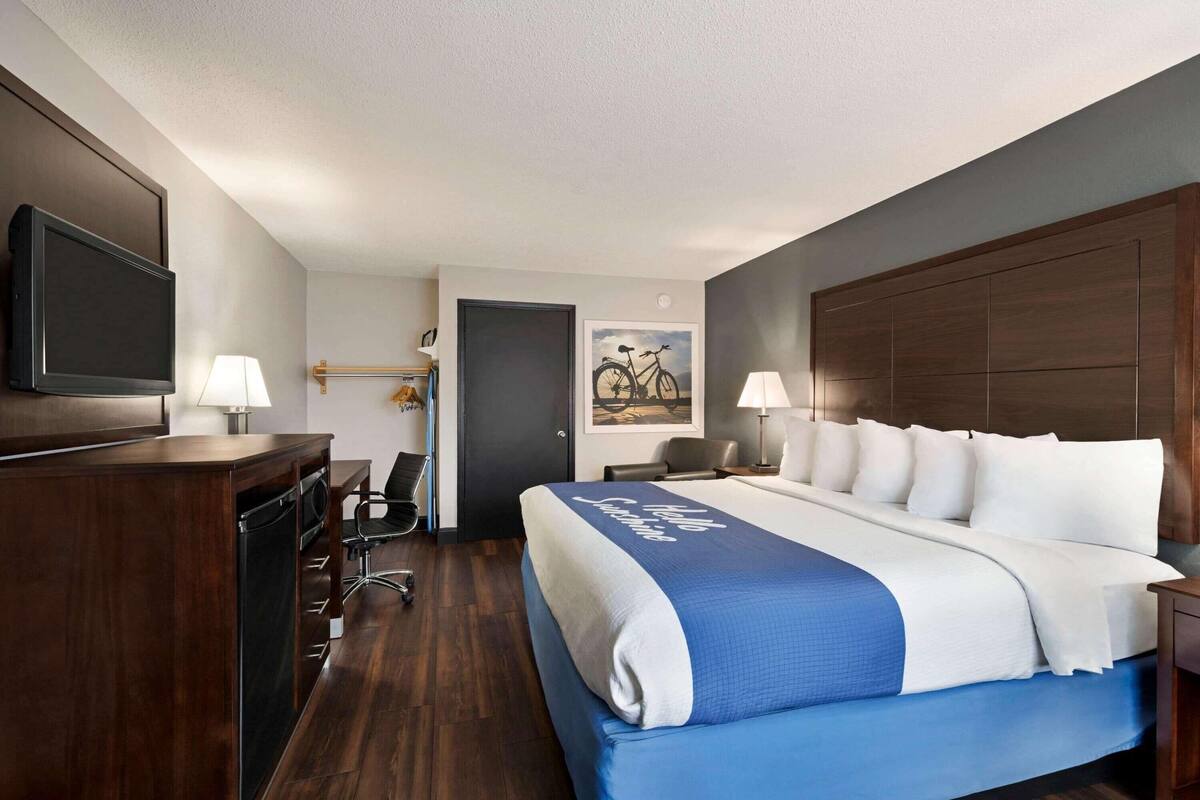 A hotel room with a bed, a desk with a chair, a television, and a door.