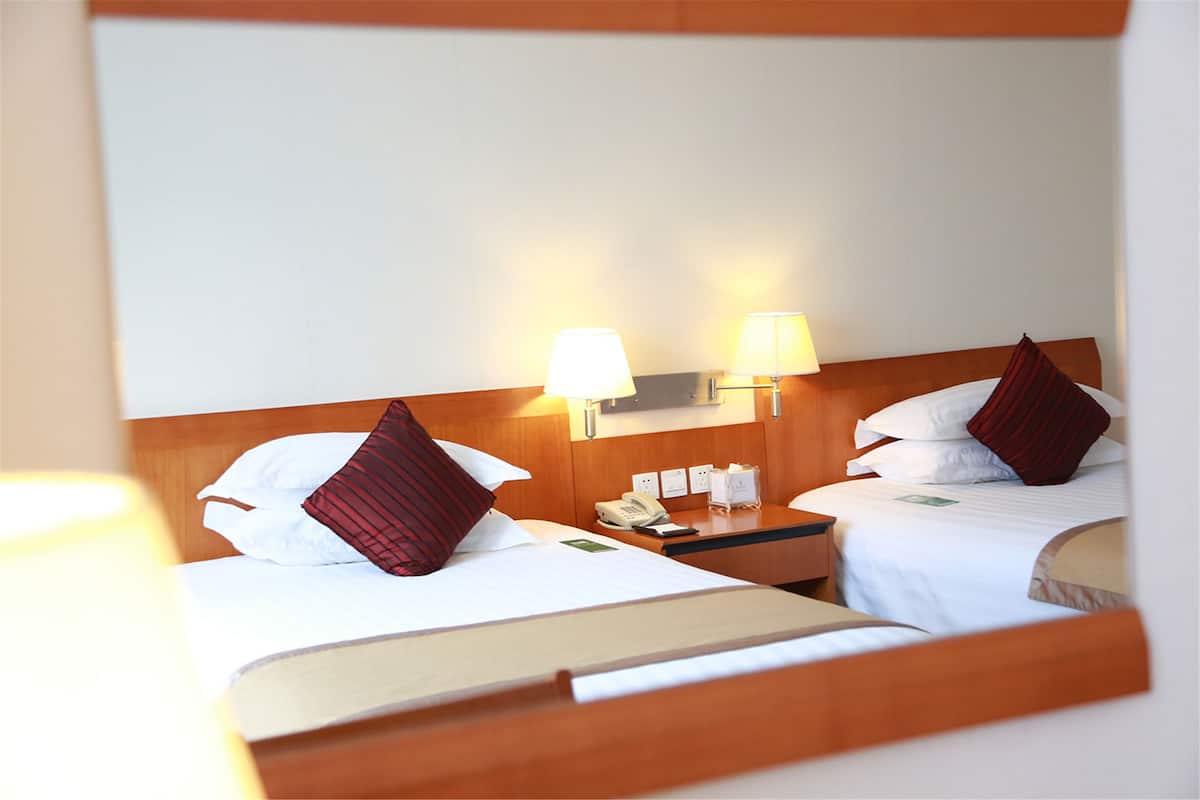 A hotel room with two beds, each with a pillow and a bedside table with a lamp.