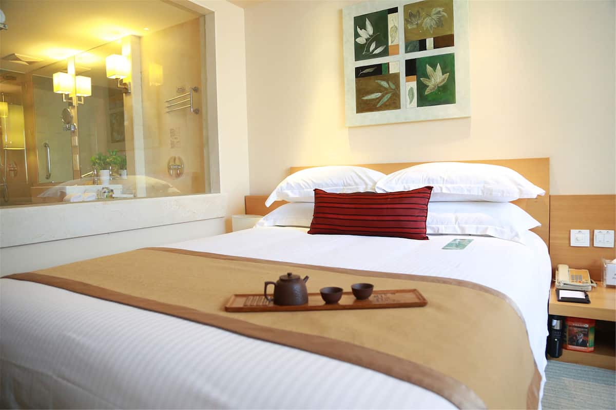 A hotel room with a bed, a bedside table with a telephone, a mirror, and a wall-mounted artwork.