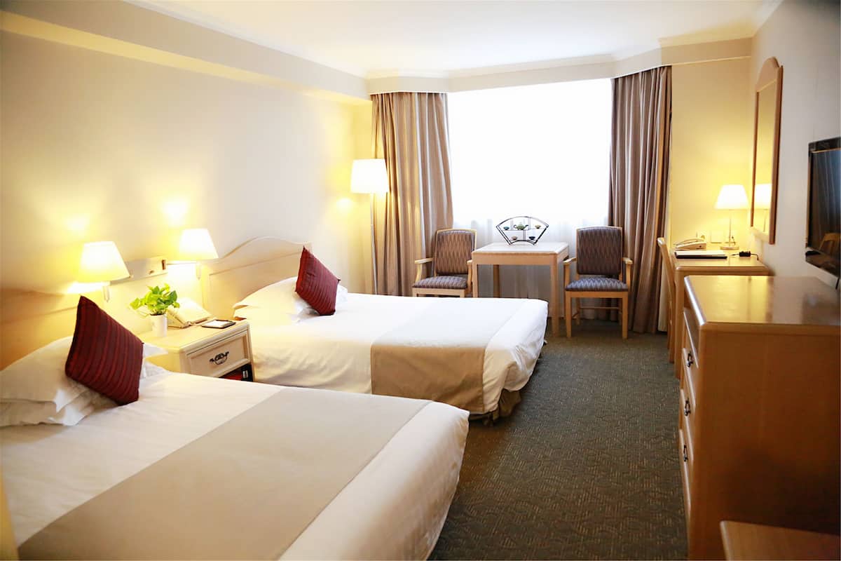 A hotel room with two beds, a desk, a chair, and a television.