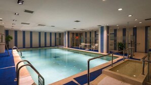 A large indoor swimming pool with clear water, surrounded by blue and beige tiled walls, and equipped with metal railings and a small hot tub area. - Jinglun Hotel Beijing (Beijing)