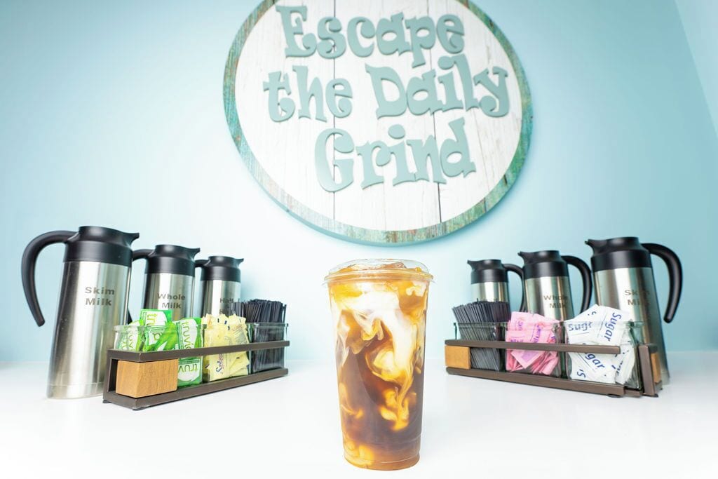 A coffee station with insulated mugs, a thermos, and a sign that reads "Escape the Daily Grind".