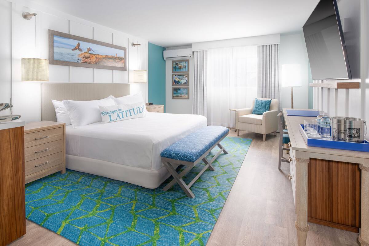 A hotel room with a bed, a desk, a chair, a TV, and artwork on the walls.