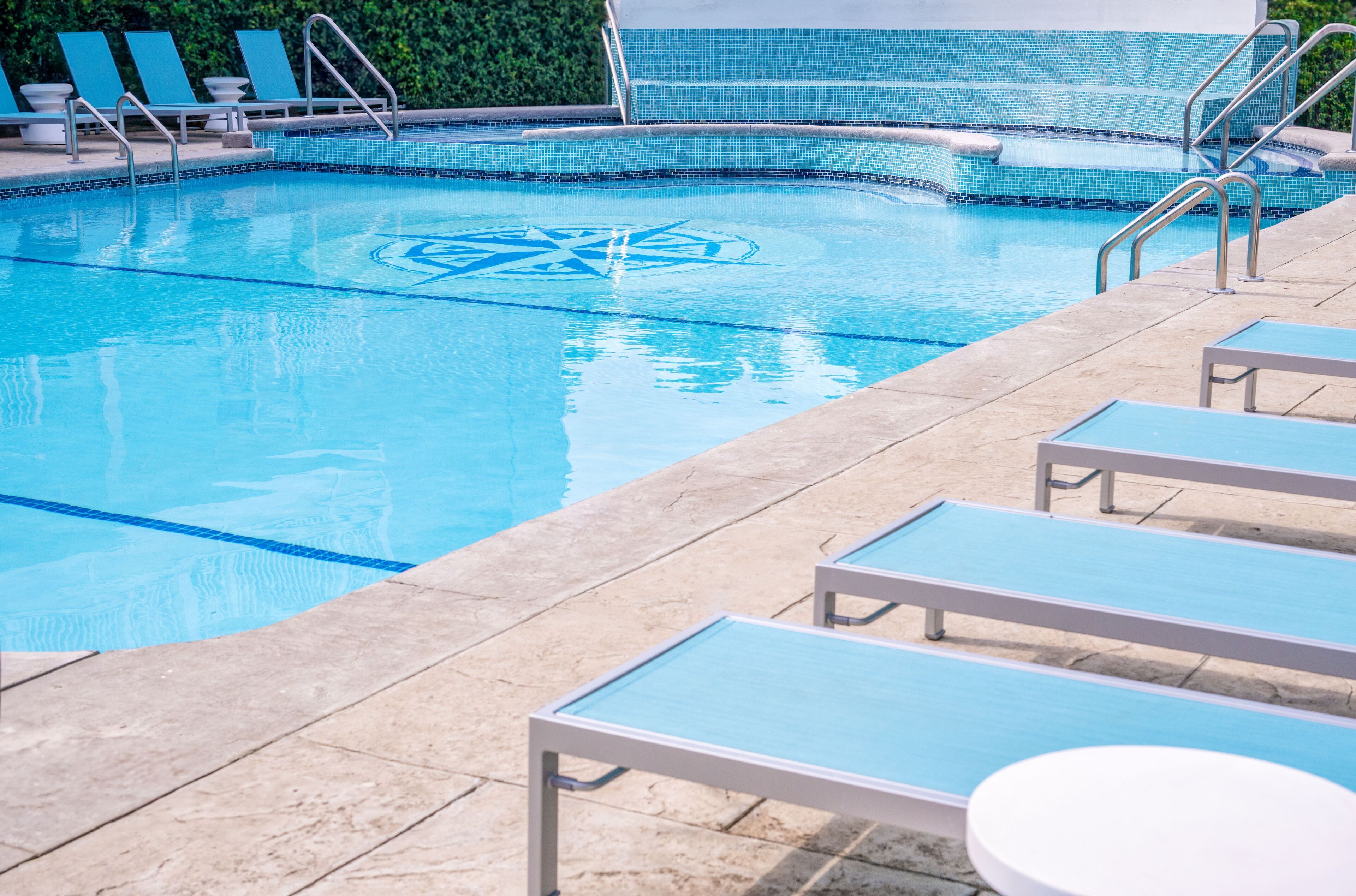 A swimming pool with lounge chairs and a tiled deck.
