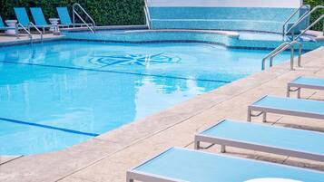 A swimming pool with lounge chairs and a tiled deck.