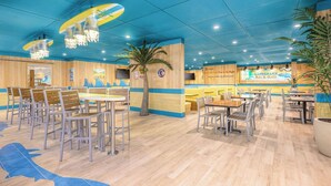 A restaurant with a blue and yellow color scheme, wooden walls, and a central palm tree. Tables and chairs are arranged for dining. - Margaritaville Resort Cape Cod (Hyannis)