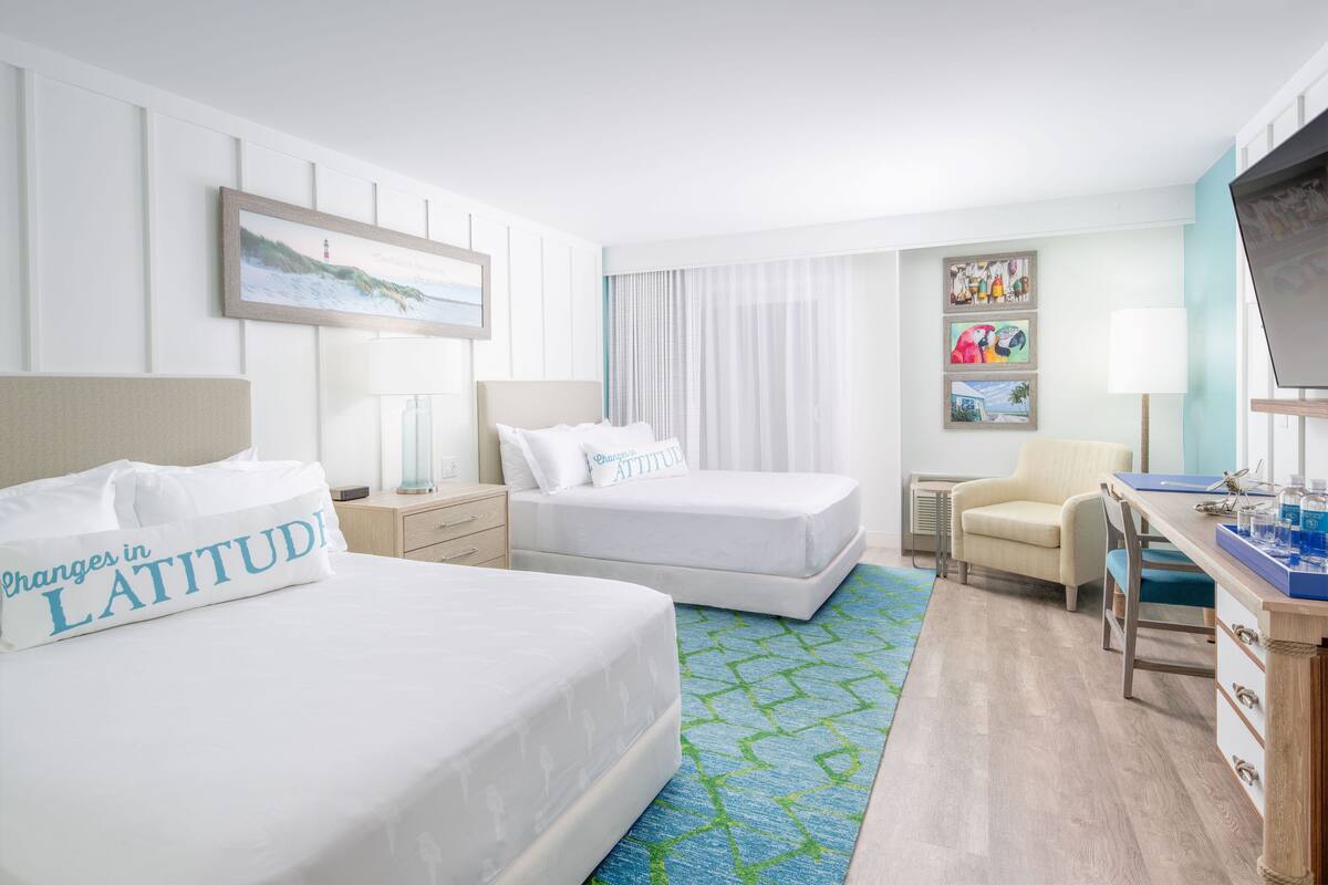 A hotel room with two beds, a desk, a chair, and a TV.