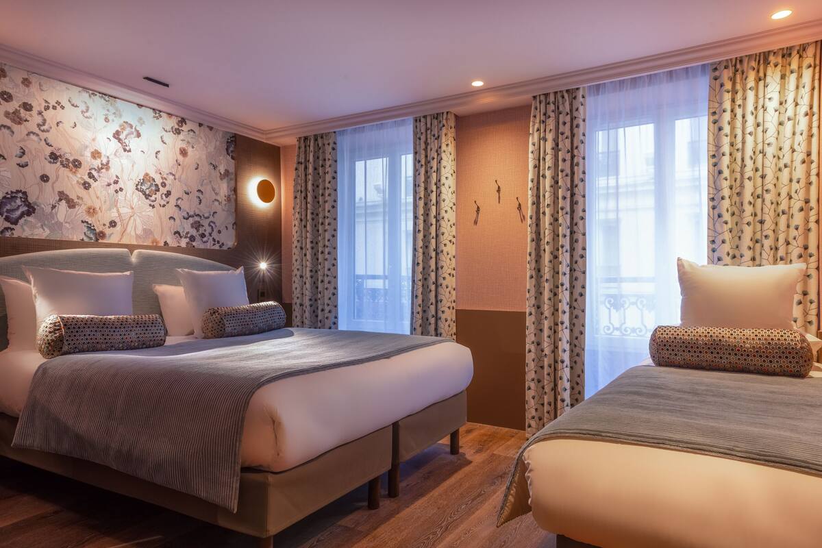 A hotel room with two beds, a large wall clock, and a window with curtains.