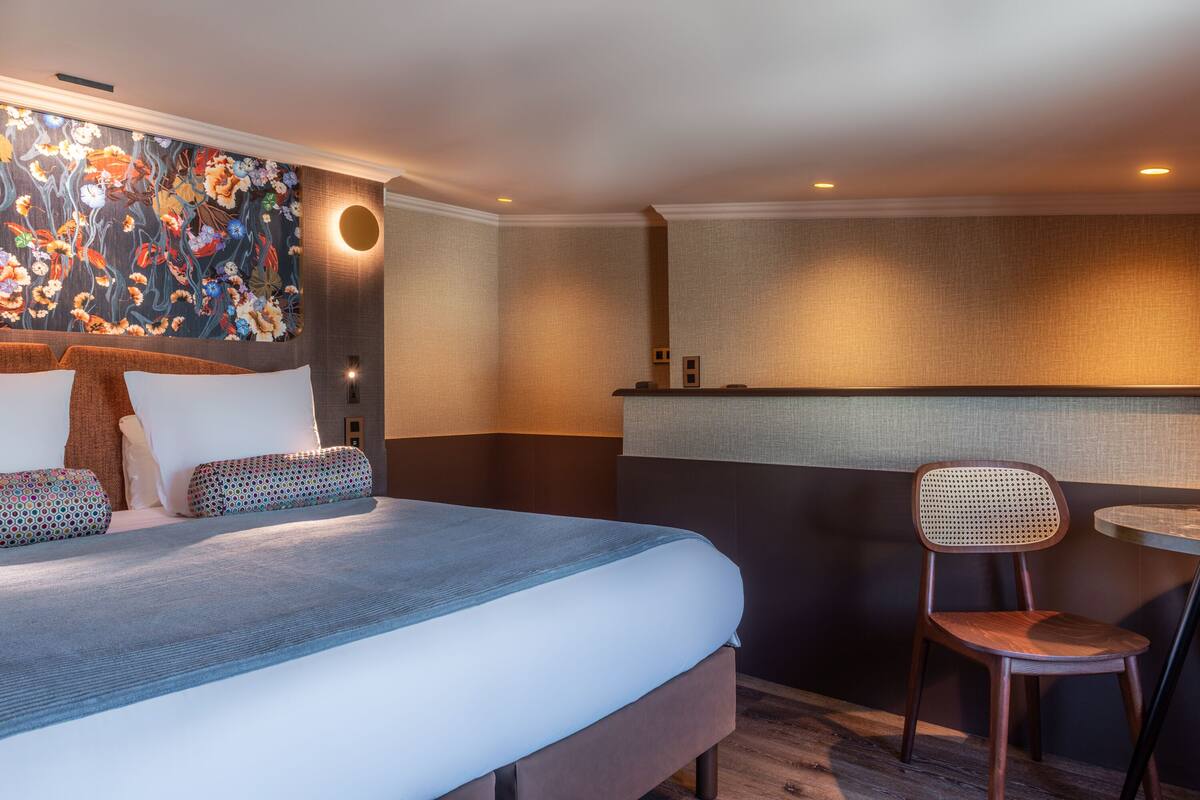A hotel room with a large bed, a chair, a small table, and a decorative wall.