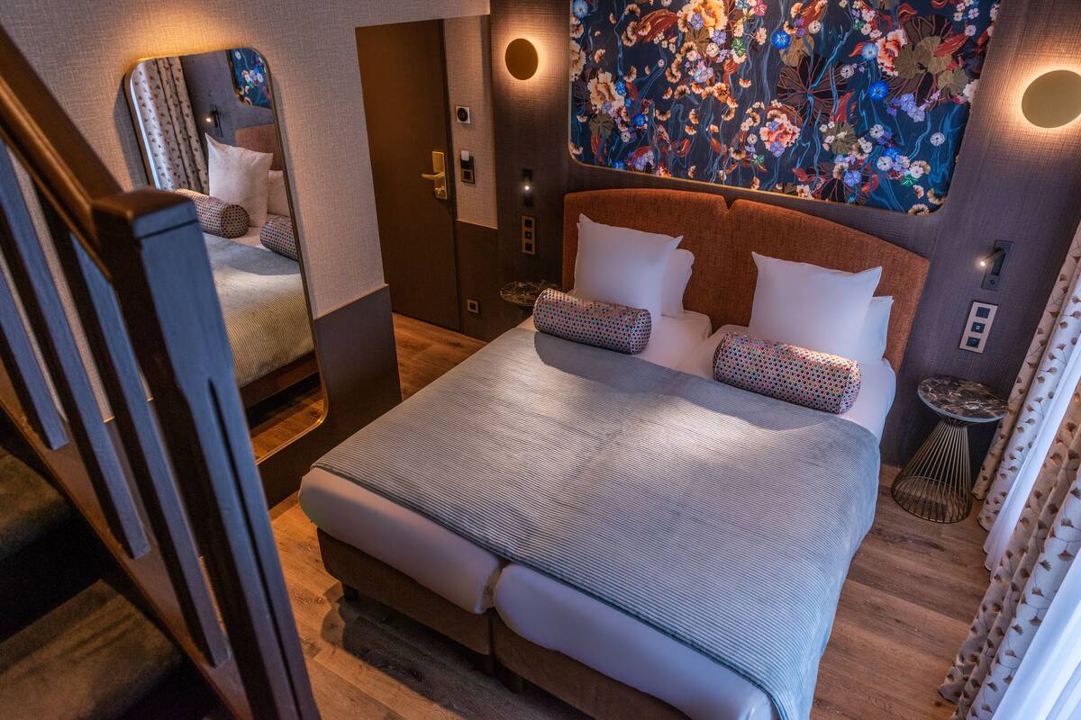 A neatly arranged bedroom with a large bed, a mirror, a small table, and a decorative wall.