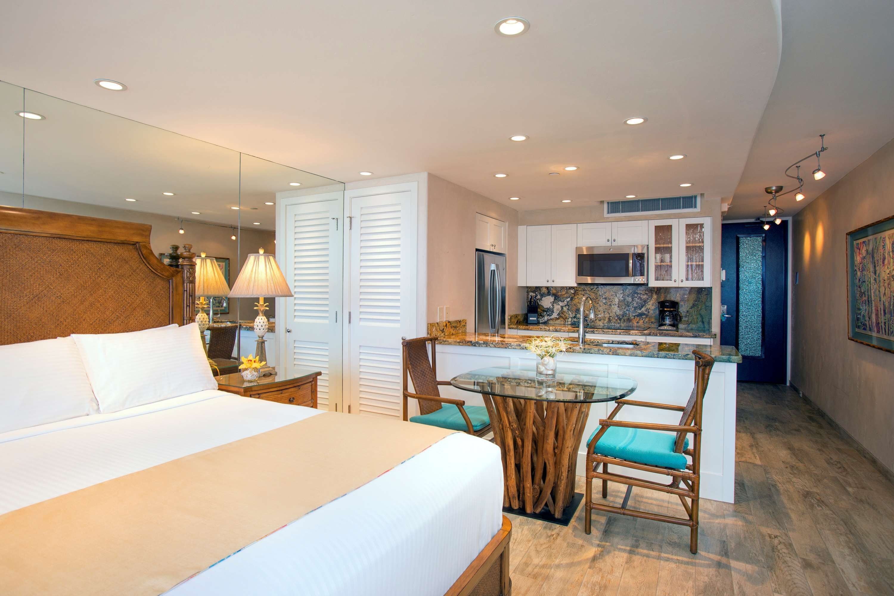 Een hotelkamer met een groot bed, een zithoek met een glazen tafel, en een kitchenette.