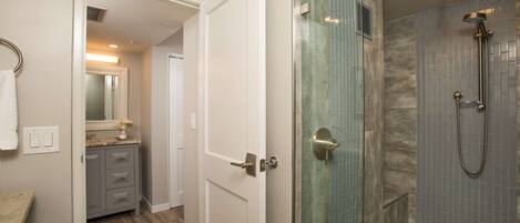 A modern bathroom with a glass-enclosed shower, a vanity with a mirror, and a door leading to another room.