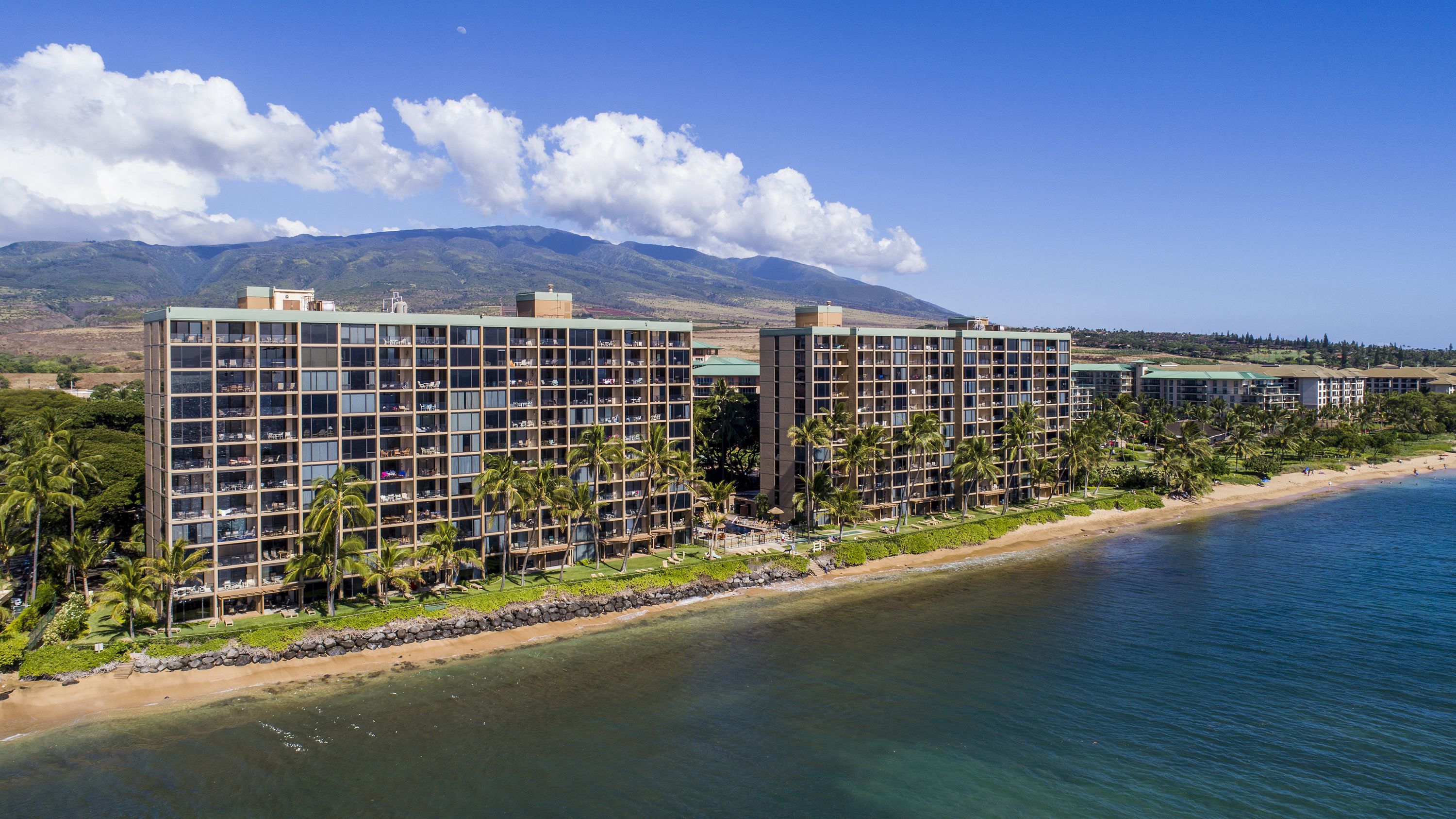 Ein Strandhotel mit mehreren Hochhäusern, einem Sandstrand und einem Berg im Hintergrund.