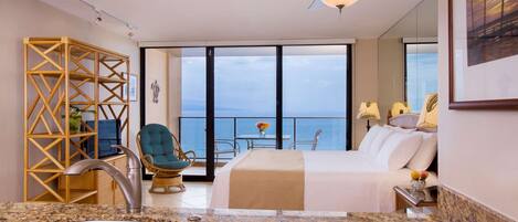 Een moderne hotelkamer met een groot bed, een balkon met uitzicht op zee, een zithoek en een badkamer met een ruime wastafel.