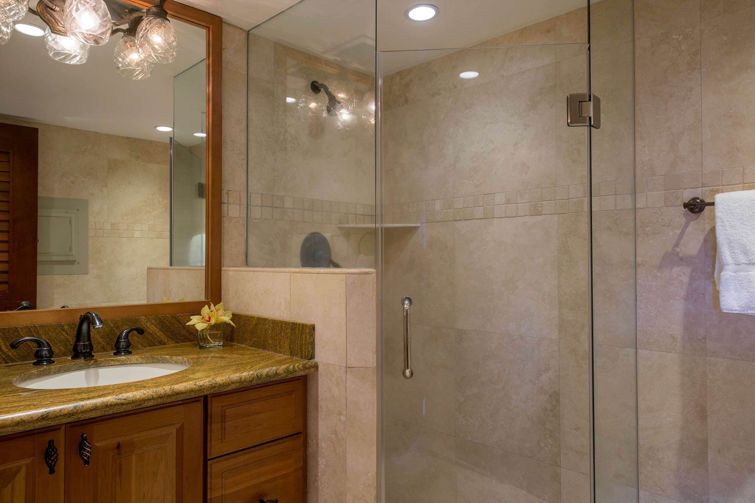 Un baño moderno con ducha de vidrio, lavamanos con encimera de mármol y muebles de madera.