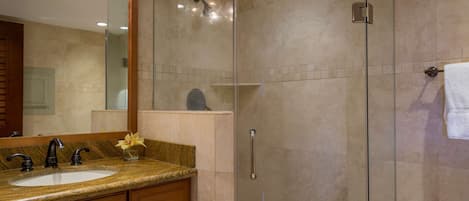 A modern bathroom with a glass-enclosed shower, a sink with a marble countertop, and wooden cabinetry.