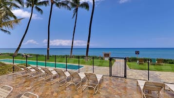A poolside area with lounge chairs, a pool, and a view of the ocean.