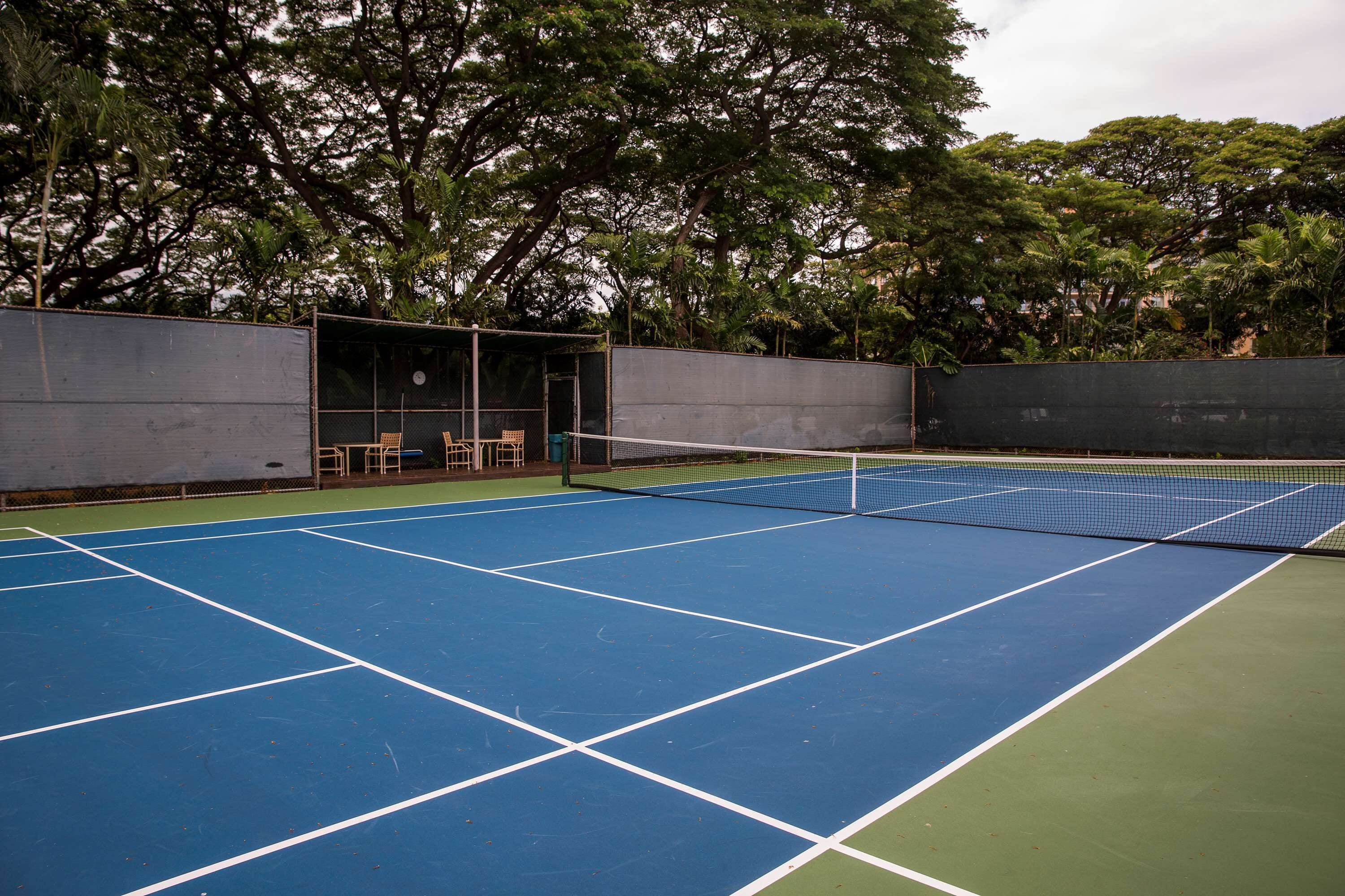 Ein Tennisplatz im Freien mit Netz, umgeben von Bäumen und einer überdachten Sitzgelegenheit.