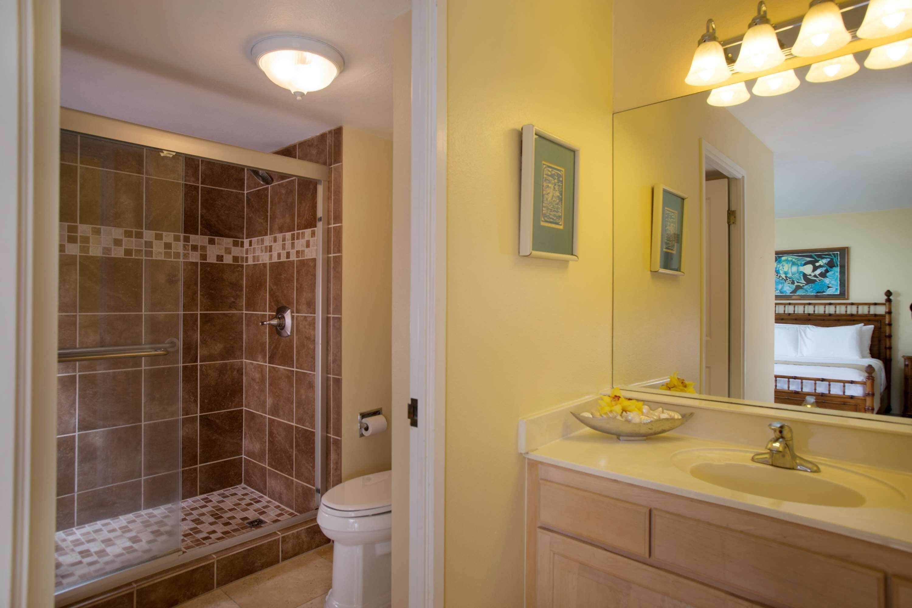 A bathroom with a shower, toilet, sink, and mirror.