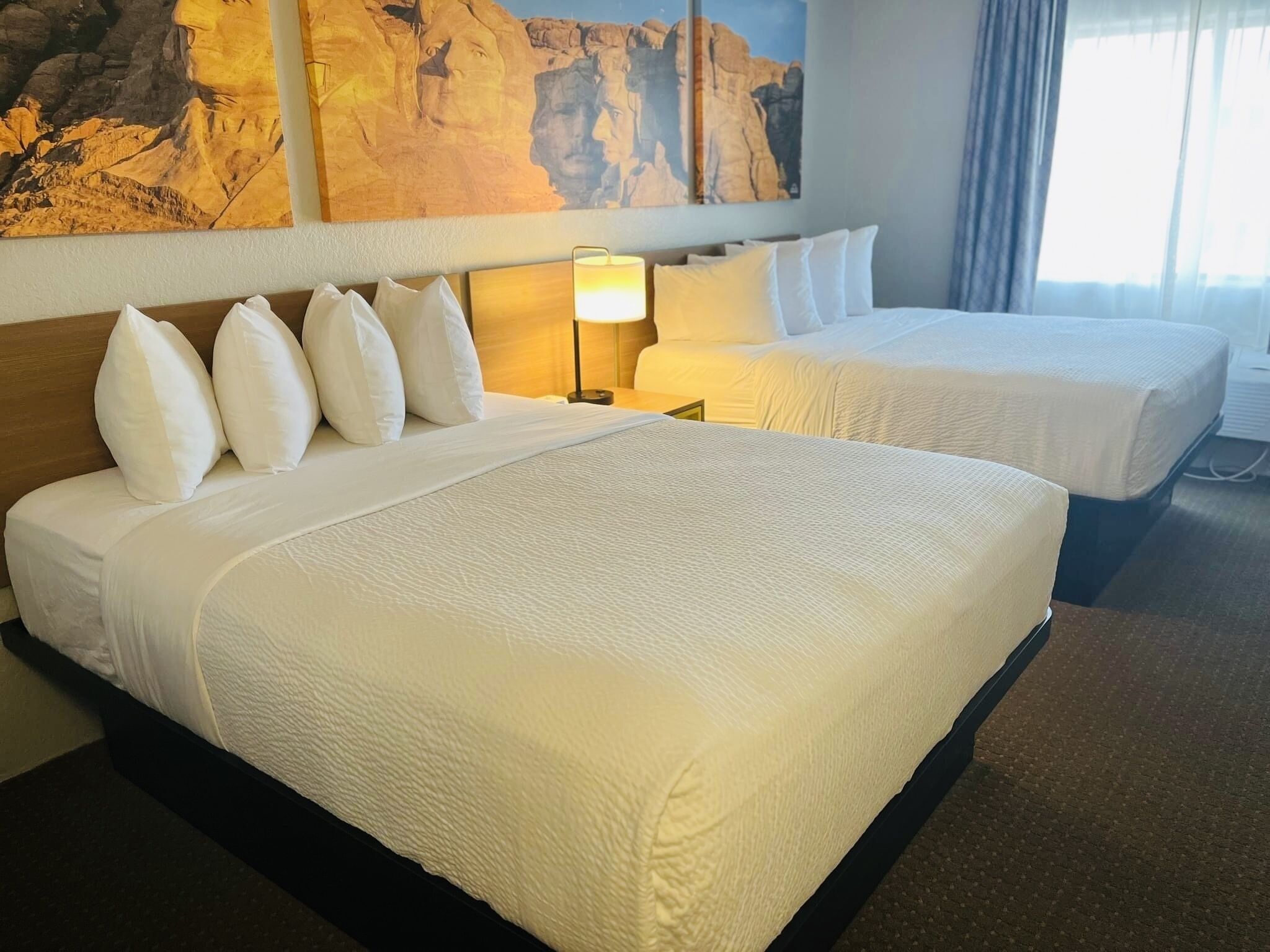 A hotel room with two beds, a large painting on the wall, and a lamp.