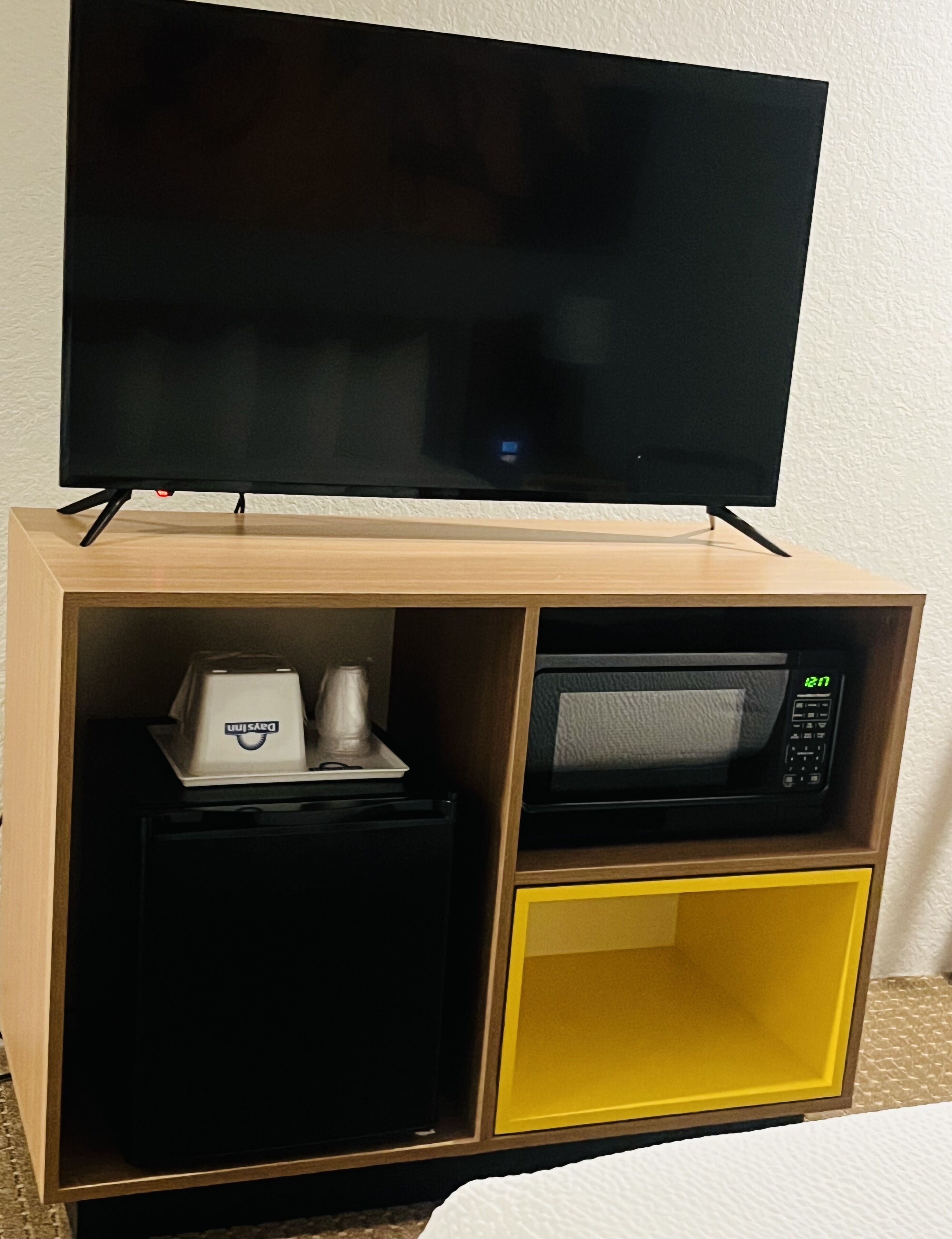 Habitación de hotel con televisor sobre un soporte de madera, microondas y refrigerador pequeño.