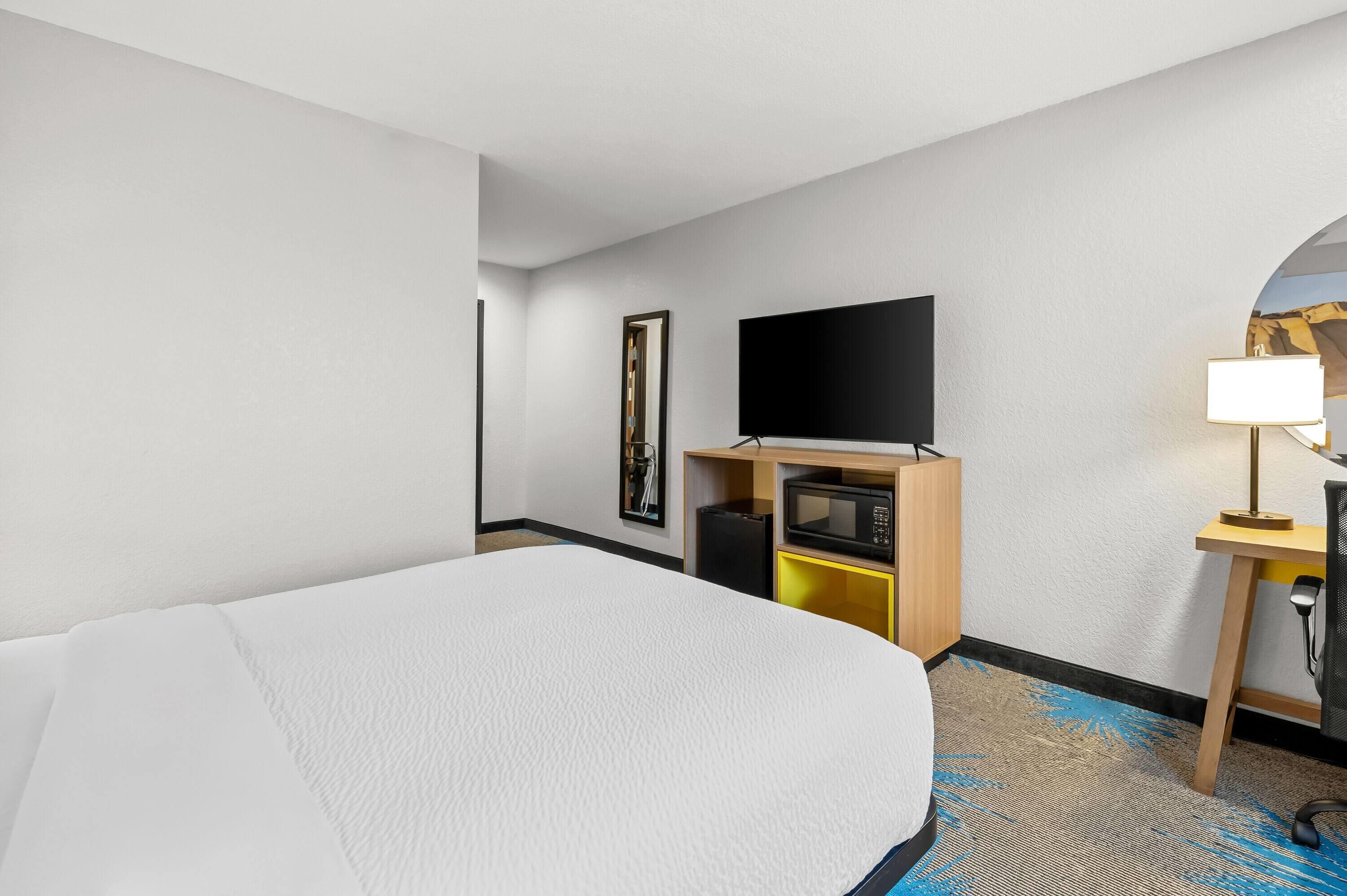 A hotel room with a large bed, a flat-screen TV, a desk with a lamp, and a microwave.
